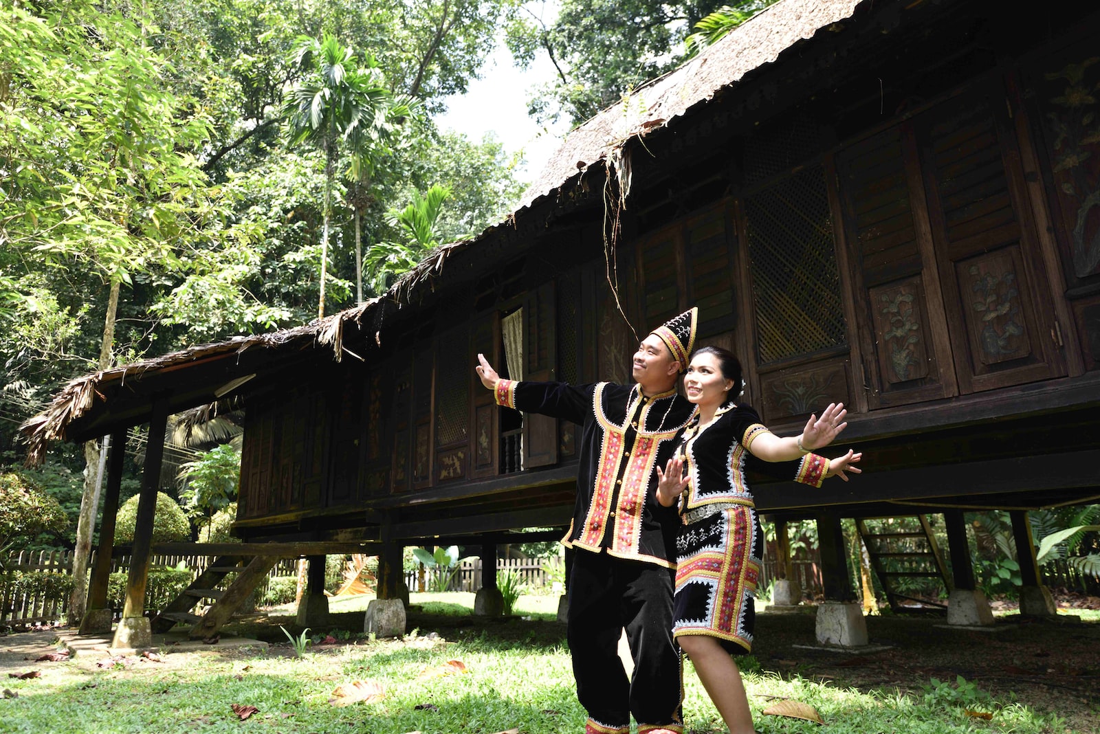 man and woman in black-and-brown matching robes standing side by side in front of wooden house
